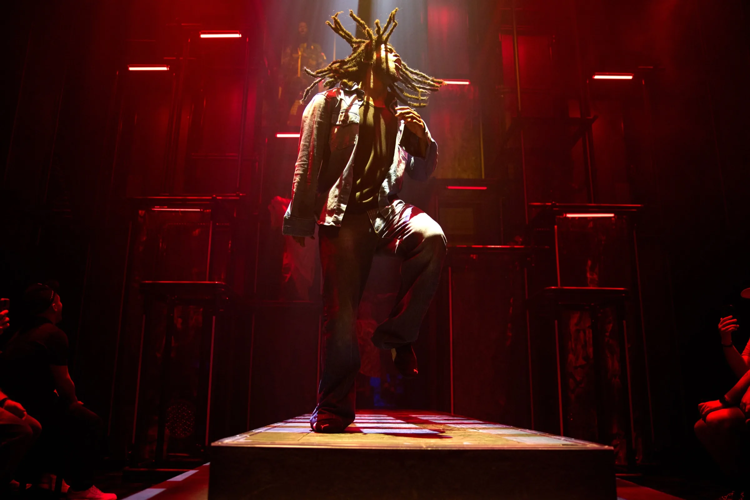 Performer mid-jump, dreads flying, lit in red